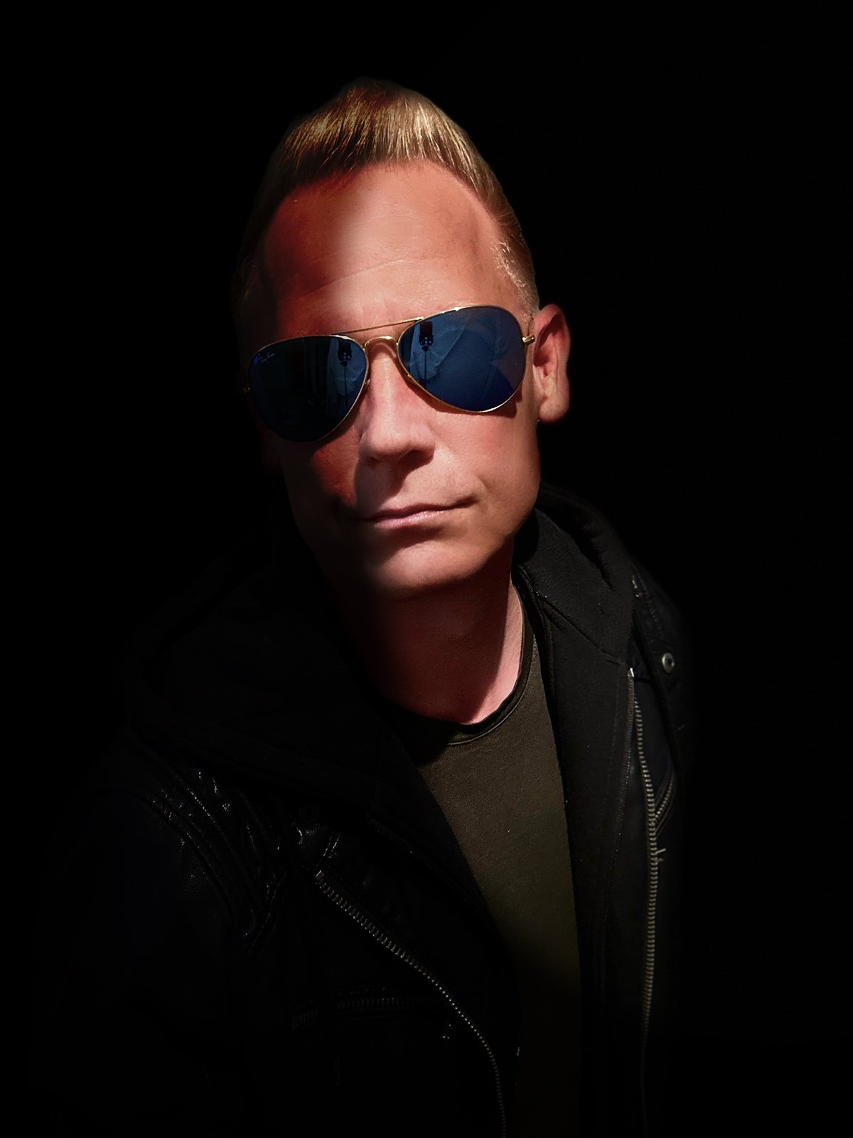 MINDLOOP in sunglasses and a dark jacket, with half his face in shadow